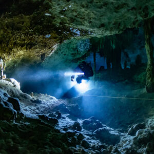 Cave diver with a bright torch above a rubble floor under a yellow ceiling, Quintana Roo, Mexico