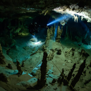 Cave diver beam crossing a chamber with dark stalagmite spikes in the foreground, Quintana Roo, Mexico