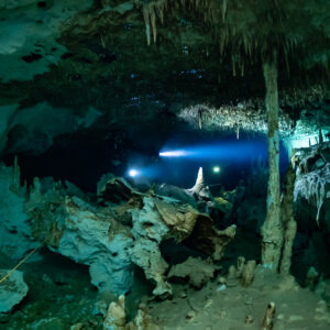 Cave divers' torches glowing beyond white columns in a turquoise chamber, Quintana Roo, Mexico