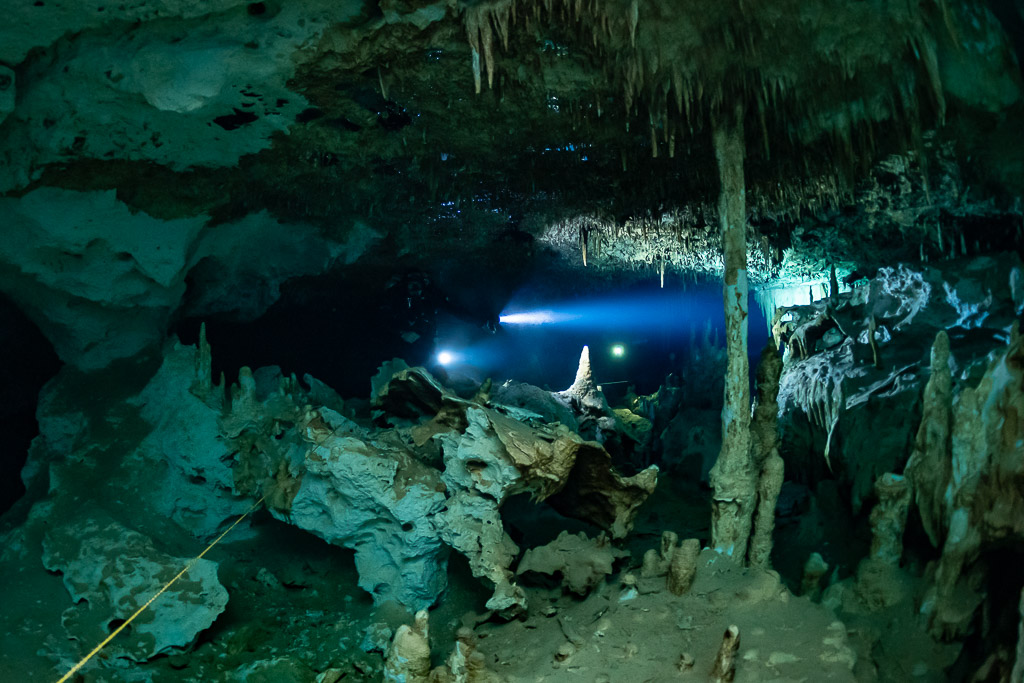 Lampes de plongeurs spéléo brillant au-delà de colonnes blanches dans une salle turquoise, Quintana Roo, Mexique