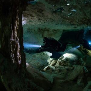 Cave diver behind a massive column with a team light in the distance, Quintana Roo, Mexico