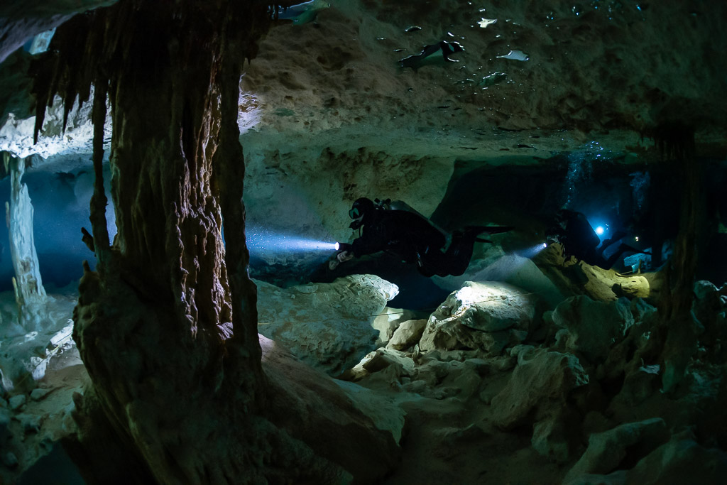 Cave diver behind a massive column with a team light in the distance, Quintana Roo, Mexico