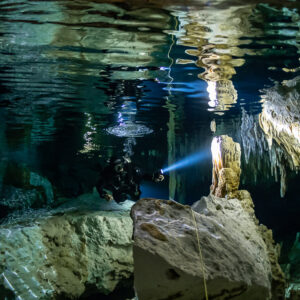 Cave diver under a mirrored air pocket ceiling reflecting the formations, Quintana Roo, Mexico