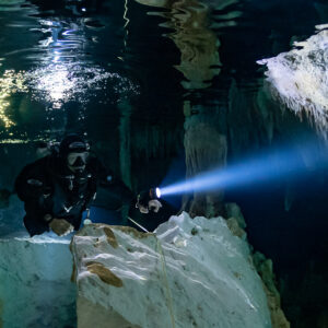 Cave diver facing the camera behind a white rock under a reflective air pocket, Quintana Roo, Mexico