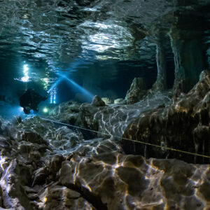 Diver beam beneath rippling air pocket reflections over jagged rock, Quintana Roo, Mexico