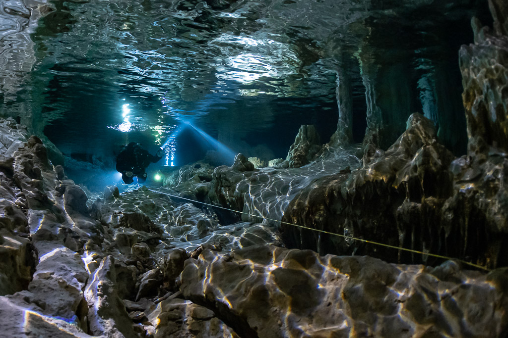 Faisceau de plongeur sous les reflets ondulants d’une poche d’air au-dessus de roches acérées, Quintana Roo, Mexique