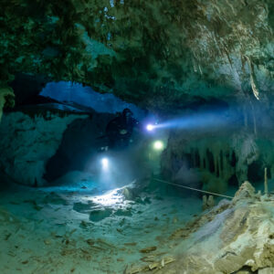 Two cave divers lighting a wide passage along a guideline over pale sand, Quintana Roo, Mexico
