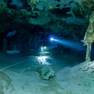 Cave diver in a turquoise passage beside a large draped stalactite, Quintana Roo, Mexico