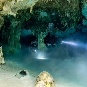 Two cave divers in a misty passage framed by pale limestone pillars, Quintana Roo, Mexico