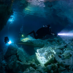 Sidemount diver with torch over white boulders in a blue cavern, Quintana Roo, Mexico