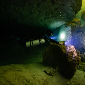 Sidemount diver illuminating boulders near a cavern entrance, Casa Cenote, Quintana Roo, Mexico