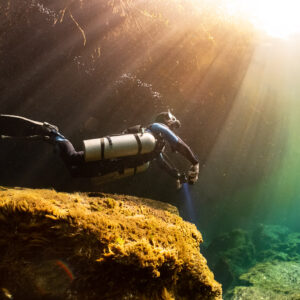 Sidemount diver over a golden rock bathed in diagonal sunlight, Casa Cenote, Quintana Roo, Mexico