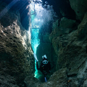 Diver in a narrow rocky crevice lit by sunbeams in a cenote, Casa Cenote, Quintana Roo, Mexico