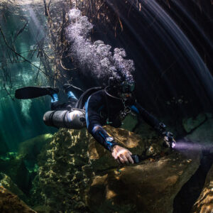 Sidemount diver with torch under bubbles and curved light rays, Casa Cenote, Quintana Roo, Mexico