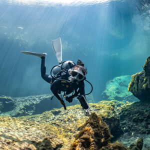 Diver approaching with fins raised over a sunlit rocky bottom, Casa Cenote, Quintana Roo, Mexico