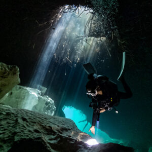 Diver lighting a cavern floor beneath a shaft of daylight, vertical, Casa Cenote, Quintana Roo, Mexico