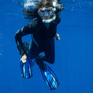 Woman snorkeler kicking down toward camera in deep blue, vertical, Tahiti, Society Islands, French Polynesia
