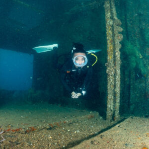 Scuba diver in a dim wreck hold beside a pillar, Baja California Sur, Mexico