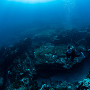 Diver exploring a dark rocky reef ledge in deep blue water, Cabo Pulmo, Baja California Sur, Mexico