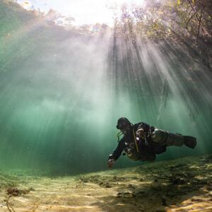 Sidemount diver under strong sunbeams in a shallow mangrove cenote, Casa Cenote, Quintana Roo, Mexico