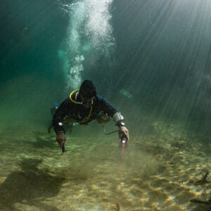 Diver with two torches swimming over sand in light-filled cenote, Casa Cenote, Quintana Roo, Mexico