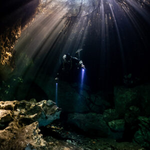 Diver with torches under sunbeams falling through a cenote opening, Casa Cenote, Quintana Roo, Mexico