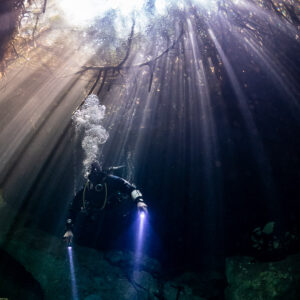Diver with bubbles and twin torch beams under cenote light shafts, Casa Cenote, Quintana Roo, Mexico