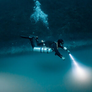 Sidemount diver gliding horizontally above the sulfide cloud with torch, Cenote Angelita, Quintana Roo, Mexico