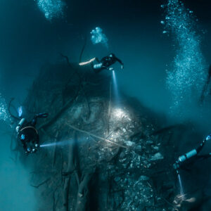 Divers with torches and bubbles around the central debris mound, Cenote Angelita, Quintana Roo, Mexico