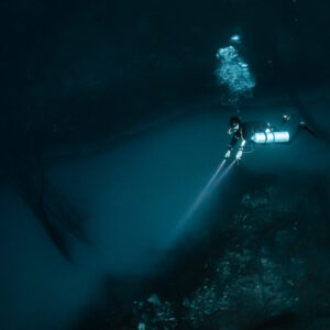 Diver with torch along the dark wall above the misty layer, Cenote Angelita, Quintana Roo, Mexico