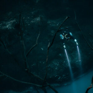 Diver with twin beams among bare branches above the cloud edge, Cenote Angelita, Quintana Roo, Mexico