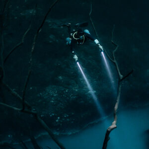 Diver above dead branches with beams reaching the misty layer, vertical, Cenote Angelita, Quintana Roo, Mexico