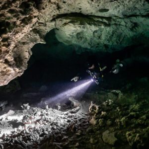 Sidemount diver lighting a low limestone passage in a cenote cavern, Quintana Roo, Mexico