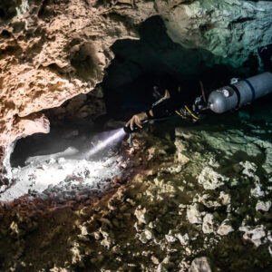 Sidemount diver with torch entering a narrow limestone overhang, Quintana Roo, Mexico