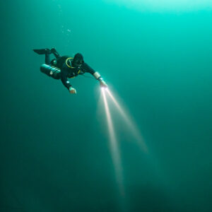 Sidemount diver with twin torches in emerald green cenote water, Quintana Roo, Mexico