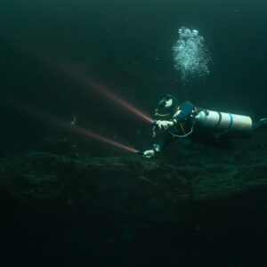 Sidemount diver with warm torch beams above a dark cenote floor, Quintana Roo, Mexico
