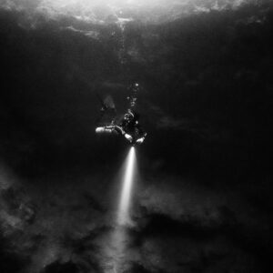 Black and white diver descending with torch into a dark cenote, Cenote El Zapote, Quintana Roo, Mexico