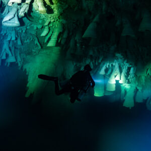 Diver lighting a curtain of bell-shaped formations in green glow, Cenote El Zapote, Quintana Roo, Mexico