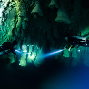 Two sidemount divers with torches beneath hanging limestone bells, Cenote El Zapote, Quintana Roo, Mexico