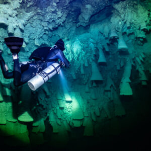 Sidemount diver close-up beside clustered limestone bells, Cenote El Zapote, Quintana Roo, Mexico