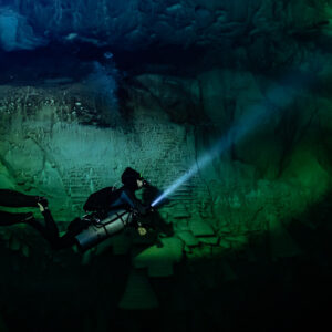 Sidemount diver beaming torch across the cenote wall below a ledge, Cenote El Zapote, Quintana Roo, Mexico