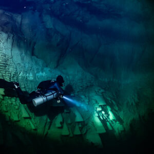 Sidemount diver beside a pale limestone wall with distant bells, Cenote El Zapote, Quintana Roo, Mexico