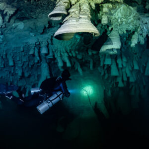 Sidemount diver under a huge pale bell formation, torch lit ahead, Cenote El Zapote, Quintana Roo, Mexico