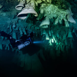 Sidemount diver lighting a distant bell under clustered limestone bells, Cenote El Zapote, Quintana Roo, Mexico
