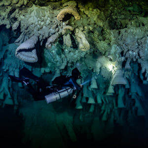 Diver passing under tilted bell formations lit by a single torch, Cenote El Zapote, Quintana Roo, Mexico