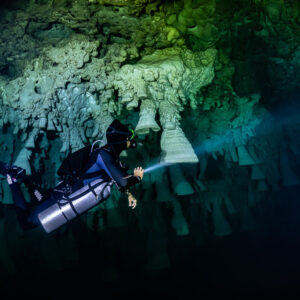 Sidemount diver close to pale bell formations with torch beam ahead, Cenote El Zapote, Quintana Roo, Mexico