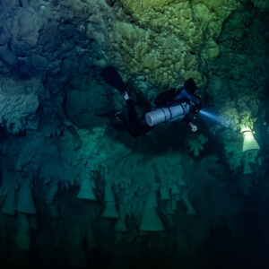 Sidemount diver in blue light lighting the base of a bell formation, Cenote El Zapote, Quintana Roo, Mexico