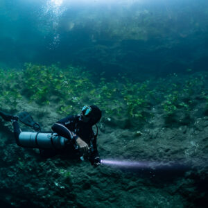 Sidemount diver lighting the slope, bubbles rising toward the surface, Quintana Roo, Mexico