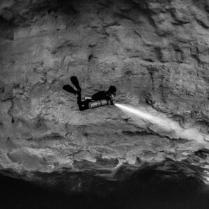 Black and white diver with torch beam against a vast rock wall, Quintana Roo, Mexico