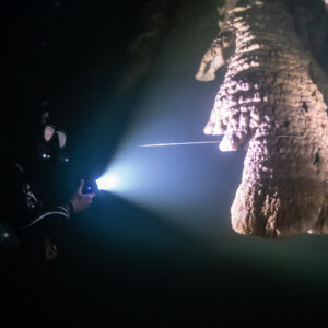 Diver lighting a large stalactite crossed by a guideline in hazy water, Quintana Roo, Mexico